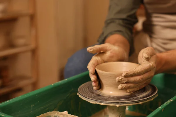 Clay crafting. Man making bowl on potter's wheel indoors, closeup. Space for text