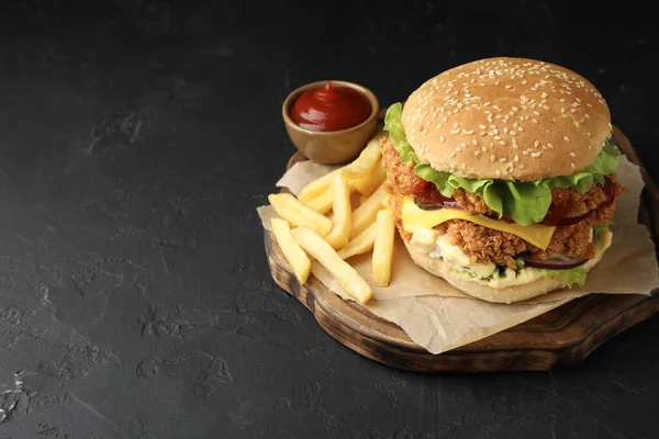 Delicious burger with crispy chicken patty, french fries and sauce on black table. Space for text