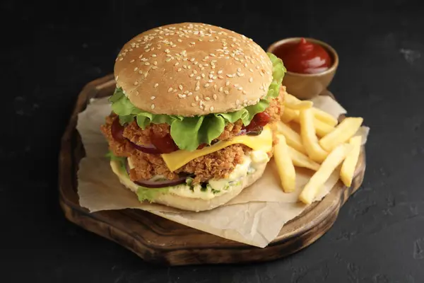 Delicious burger with crispy chicken patty, french fries and sauce on black table
