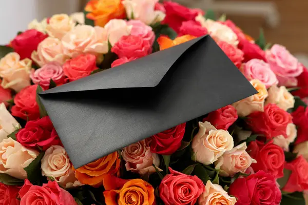 Black envelope on bouquet of beautiful roses, closeup