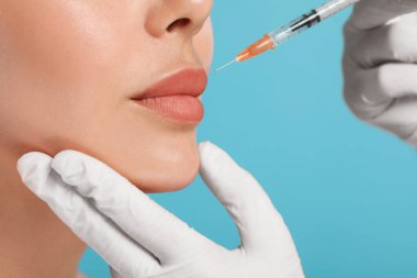 Doktor açık mavi arka planda genç bayana dudak iğnesi yapıyor, yakın plan. Estetik ameliyat