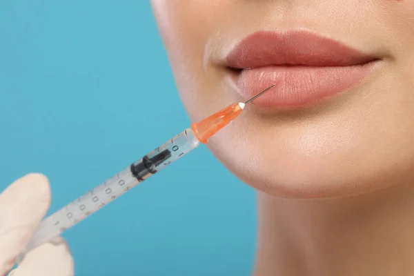 stock image Doctor giving lips injection to young woman on light blue background, closeup. Cosmetic surgery