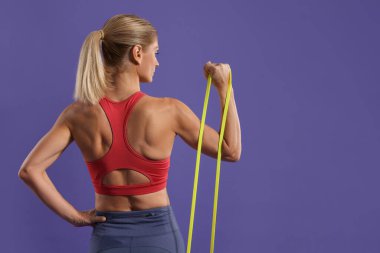 Atletik kadın mor arka planda elastik direniş bandıyla egzersiz yapıyor. Metin için boşluk