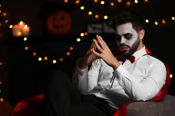 Man in scary vampire costume against blurred lights indoors, space for text. Halloween celebration