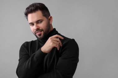 Gri arka planda şık siyah süveter giyen yakışıklı bir adam.