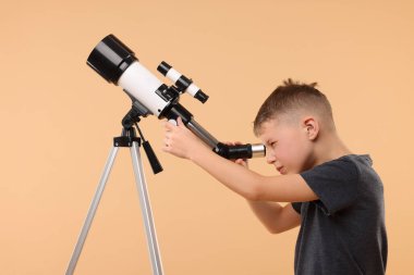 Bej arka planda teleskopla yıldızlara bakan küçük bir çocuk.