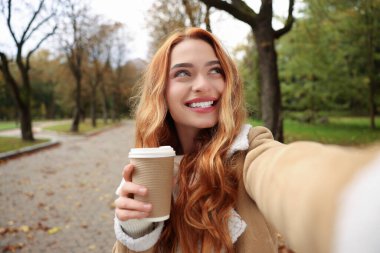 Sonbahar parkında kağıt bardakla selfie çeken mutlu kadın portresi.