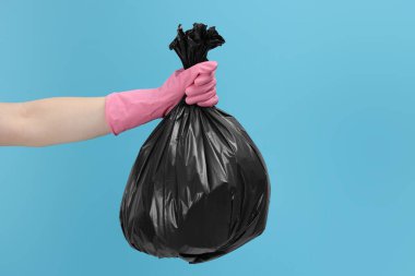 Açık mavi arka planda çöp dolu plastik poşet taşıyan kadın, yakın plan.