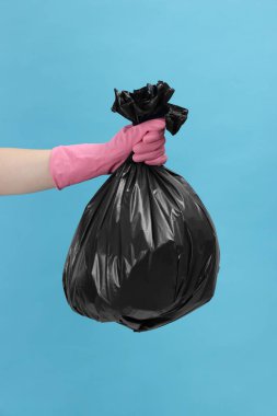 Açık mavi arka planda çöp dolu plastik poşet taşıyan kadın, yakın plan.