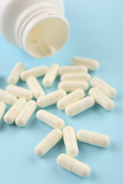 Açık mavi arka planda şişe ve vitamin kapsülleri, yakın plan