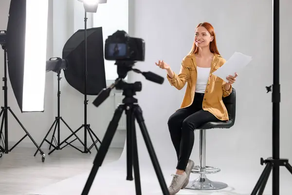 Casting call. Woman with script performing in front of camera against light grey background at studio