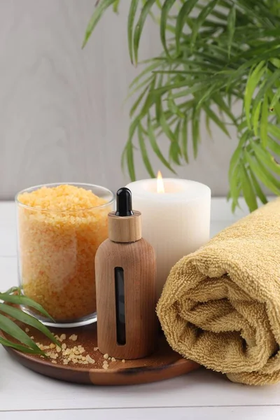 Spa composition. Bottle of cosmetic product, sea salt, burning candle and towel on white table