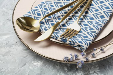 Temiz tabaklar, çatal bıçak takımı, peçete ve lavanta çiçekleri açık gri desenli masa, yakın plan.