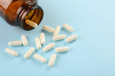 Açık mavi arka planda şişe ve vitamin kapsülleri, yakın plan. Metin için boşluk