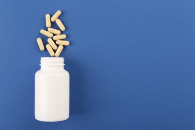 Mavi arka planda şişe ve vitamin kapsülleri, üst manzara. Metin için boşluk