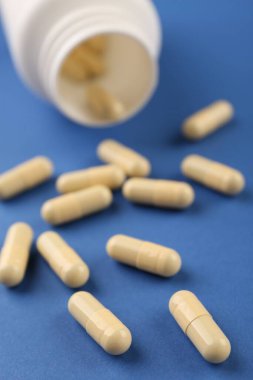 Mavi arka planda şişe ve vitamin kapsülleri, yakın plan