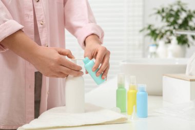 Banyodaki beyaz tezgahta plastik şişeye kozmetik ürünler döken bir kadın. Banyo aksesuarları