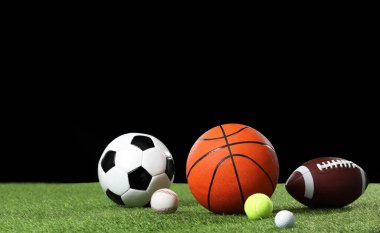 Siyah arkaplana karşı yeşil çimenler üzerinde birçok farklı spor topu, metin için boşluk