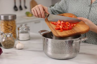 Yemek pişirme süreci. Mutfaktaki beyaz mermer masada biber ekleyen kadın, yakın plan.