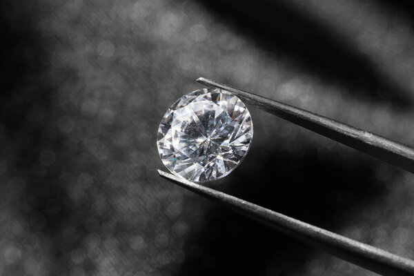 Tweezers with beautiful shiny diamond on dark background, closeup