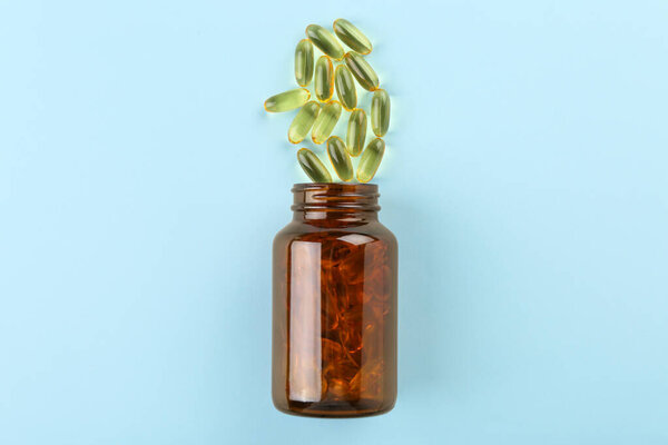 Bottle and vitamin capsules on light blue background, top view