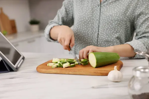Cooking process. Woman cutting zucchini at white marble countertop, closeup