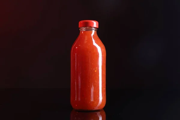 Spicy chili sauce in bottle on against dark background