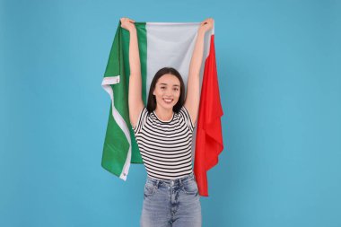 Açık mavi arka planda İtalya bayrağı taşıyan genç bir kadın