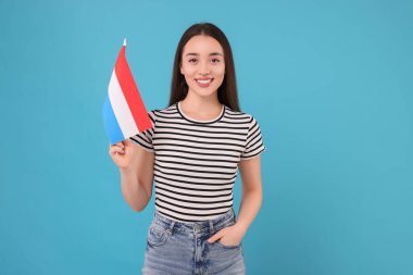 Açık mavi arka planda Hollanda bayrağı taşıyan genç bir kadın.