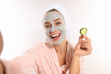 Yüz maskeli ve salatalık dilimli bir kadın beyaz arka planda selfie çekiyor. Spa tedavileri