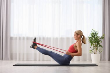 Spor yapan atletik bir kadın evde spor yaparken lastikli bant takıyor.