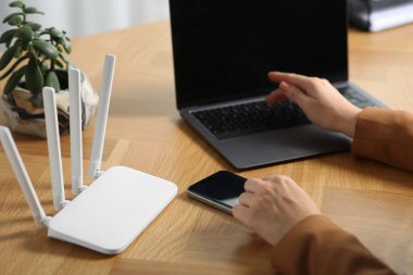 Akıllı telefonu ve bilgisayarı olan bir kadın internete Wi-Fi yönlendiricisiyle bağlanıyor.