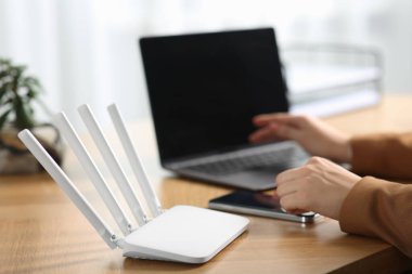 Akıllı telefonu ve bilgisayarı olan bir kadın internete Wi-Fi yönlendiricisiyle bağlanıyor.