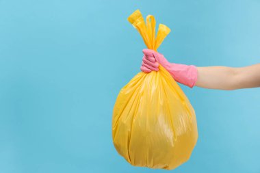 Açık mavi arka planda çöp dolu plastik poşet taşıyan bir kadın, yakın plan. Metin için boşluk