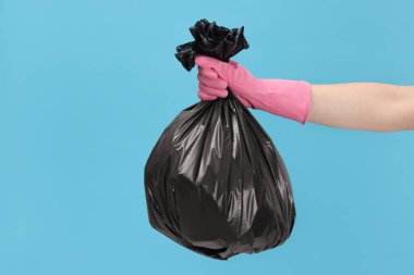 Açık mavi arka planda çöp dolu plastik poşet taşıyan kadın, yakın plan.