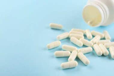 Açık mavi arka planda şişe ve vitamin kapsülleri, yakın plan. Metin için boşluk