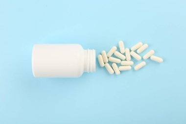 Açık mavi zemin üzerinde şişe ve vitamin kapsülleri, üst görünüm