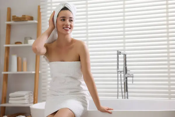 Smiling young woman near tub after shower in bathroom