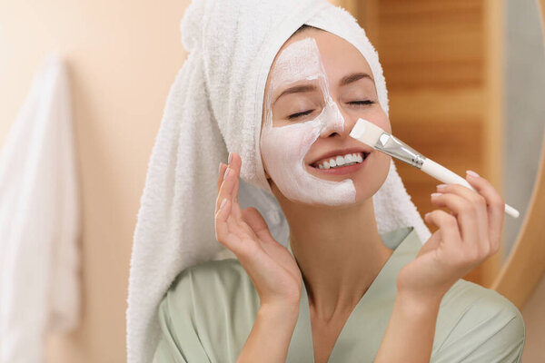 Woman applying face mask indoors. Spa treatments