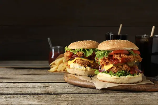 Delicious burgers with crispy chicken patty, french fries and soda drinks on wooden table. Space for text