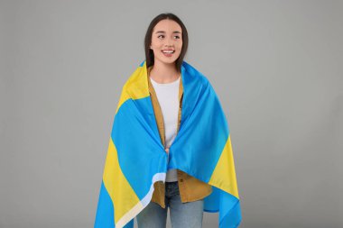 Açık gri arka planda İsveç bayrağı taşıyan genç bir kadın.