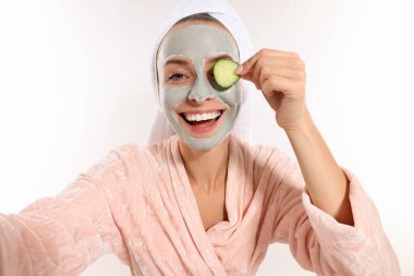 Yüz maskeli ve salatalık dilimli bir kadın beyaz arka planda selfie çekiyor. Spa tedavileri