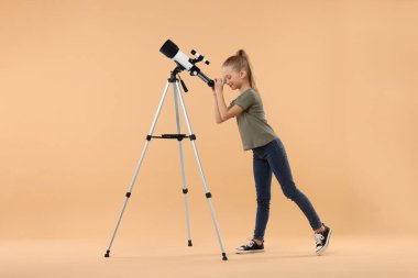 Bej arkaplanda teleskopla yıldızlara bakan küçük kız