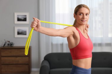 Spor yapan atletik kadın evde spor lastiğiyle egzersiz yapıyor.