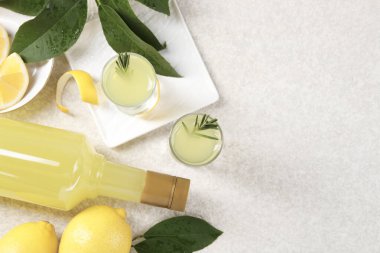 Lezzetli limoncello likörü, limon ve yeşil yapraklar açık dokulu masa, düz yatak. Metin için boşluk