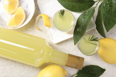 Lezzetli limoncello likörü, limonlar ve yeşil yapraklar açık dokulu masa, düz yatıyordu.