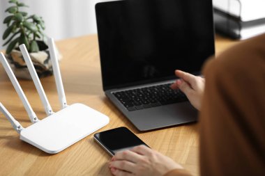 Akıllı telefonu ve bilgisayarı olan bir kadın internete Wi-Fi yönlendiricisiyle bağlanıyor.