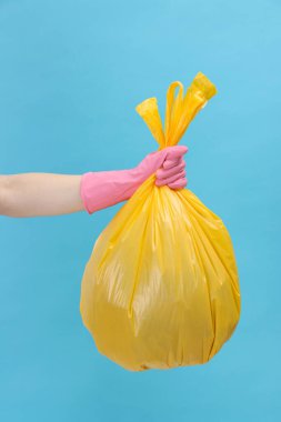 Açık mavi arka planda çöp dolu plastik poşet taşıyan kadın, yakın plan.