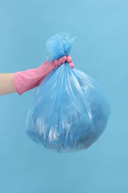Açık mavi arka planda çöp dolu plastik poşet taşıyan kadın, yakın plan.