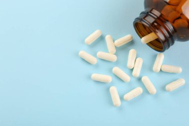 Açık mavi zemin üzerinde şişe ve vitamin kapsülleri. Metin için boşluk